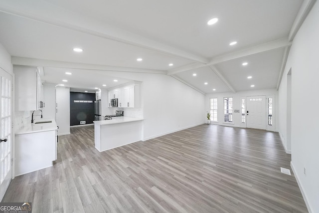 unfurnished living room featuring sink, lofted ceiling with beams, and light hardwood / wood-style flooring