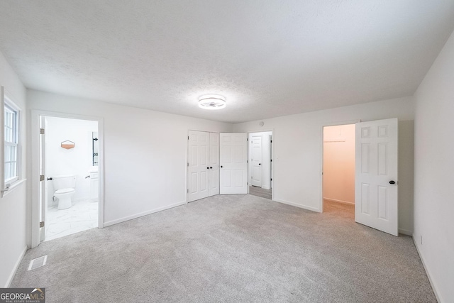 unfurnished bedroom featuring connected bathroom, light colored carpet, and a textured ceiling