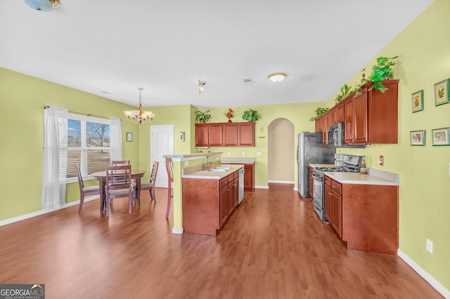 kitchen with hardwood / wood-style floors, pendant lighting, an island with sink, sink, and stainless steel appliances