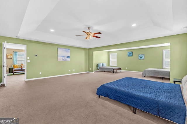 carpeted bedroom featuring ceiling fan and a tray ceiling