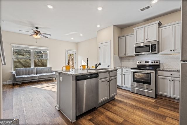 kitchen with stainless steel appliances, an island with sink, gray cabinetry, and decorative backsplash