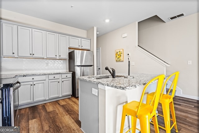 kitchen featuring sink, a breakfast bar, appliances with stainless steel finishes, light stone countertops, and decorative backsplash