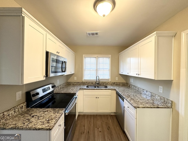 kitchen with sink, dark wood-type flooring, stainless steel appliances, light stone countertops, and white cabinets