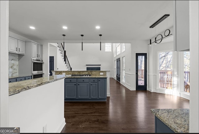 kitchen featuring appliances with stainless steel finishes, dark wood-type flooring, pendant lighting, and light stone counters