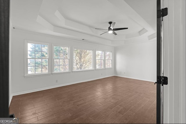 empty room with dark hardwood / wood-style flooring, a raised ceiling, and ceiling fan