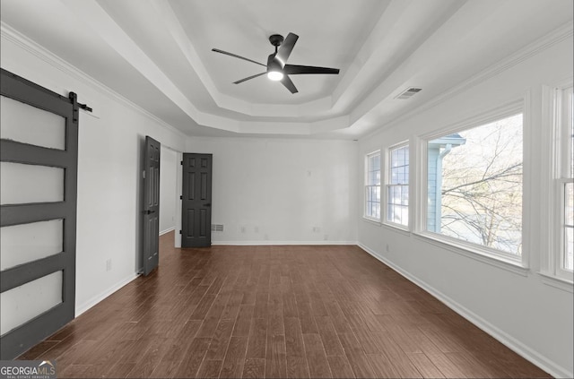 spare room with crown molding, ceiling fan, a raised ceiling, dark hardwood / wood-style flooring, and a barn door