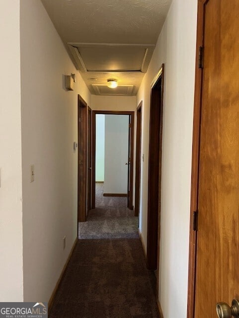 hallway featuring a textured ceiling and dark carpet