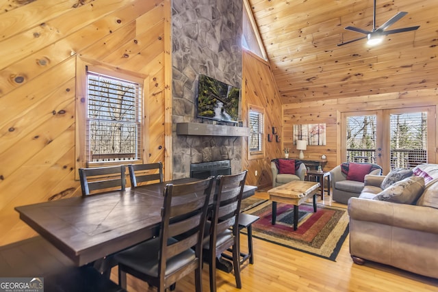 dining area featuring hardwood / wood-style flooring, wooden walls, high vaulted ceiling, a fireplace, and wooden ceiling