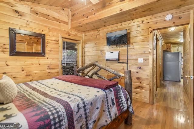 bedroom featuring hardwood / wood-style flooring, wooden walls, wood ceiling, and stainless steel refrigerator