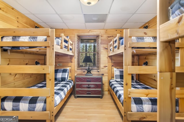 bedroom with hardwood / wood-style flooring, wood walls, and a drop ceiling