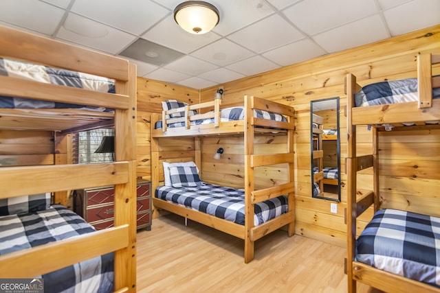 bedroom featuring a paneled ceiling, wood-type flooring, and wood walls