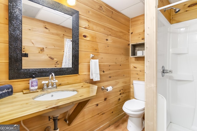 bathroom with a shower, sink, wooden walls, and toilet