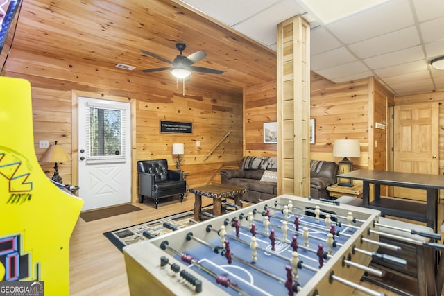 rec room with a drop ceiling, wooden walls, ceiling fan, and light wood-type flooring