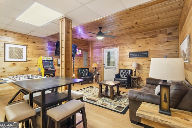 living room featuring ceiling fan, wood walls, wood-type flooring, and a drop ceiling