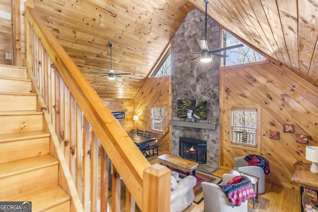 unfurnished living room featuring wood ceiling, ceiling fan, wooden walls, high vaulted ceiling, and a stone fireplace