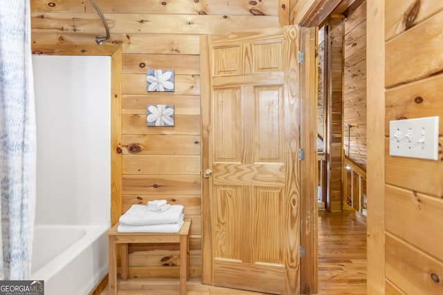 interior space featuring hardwood / wood-style floors, a bath, and wooden walls