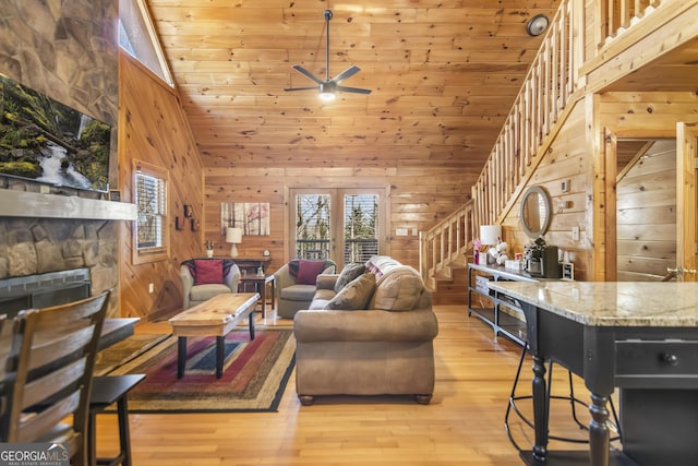 living room with wooden walls, high vaulted ceiling, a fireplace, light hardwood / wood-style floors, and wooden ceiling