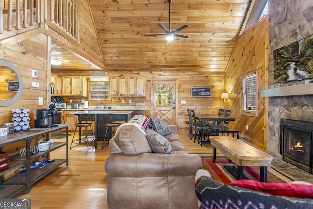 living room featuring light hardwood / wood-style flooring, wooden walls, high vaulted ceiling, a stone fireplace, and wooden ceiling