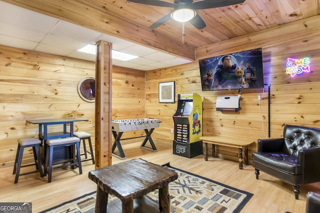 living area with hardwood / wood-style floors, ceiling fan, and wood walls