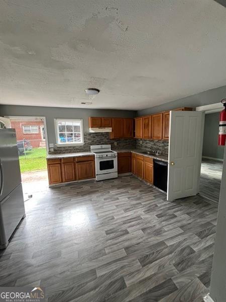 4402 Highland Rd, Decatur, GA 30035 - kitchen with white stove, freestanding refrigerator, a textured ceiling, backsplash, and under cabinet range hood