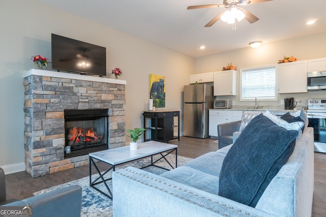 living room featuring ceiling fan, a fireplace, dark hardwood / wood-style flooring, and sink