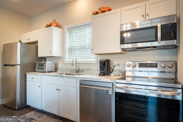 kitchen with appliances with stainless steel finishes, white cabinetry, sink, dark hardwood / wood-style flooring, and light stone counters