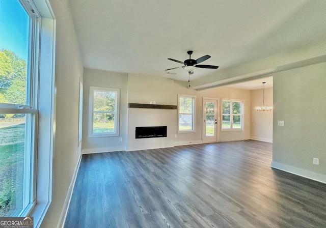 unfurnished living room with dark wood-type flooring, plenty of natural light, and ceiling fan with notable chandelier