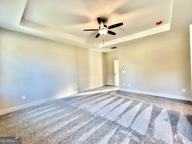 spare room with ceiling fan, a raised ceiling, and carpet