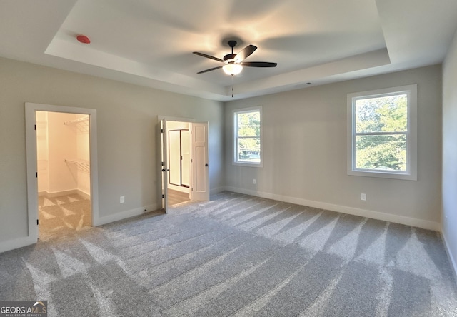 unfurnished bedroom with a spacious closet, light colored carpet, a raised ceiling, and ceiling fan