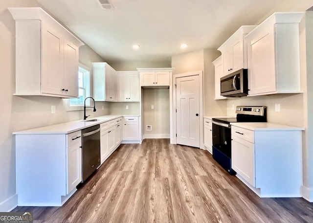 kitchen with white cabinetry, appliances with stainless steel finishes, sink, and light wood-type flooring