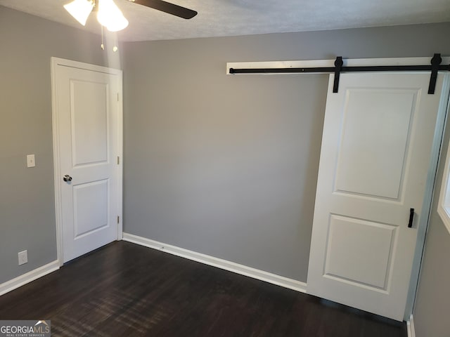 unfurnished bedroom with a barn door, dark wood-type flooring, a textured ceiling, and ceiling fan