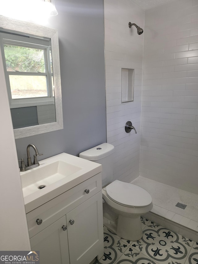 bathroom with tile patterned flooring, vanity, toilet, and a tile shower