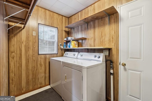 laundry room with separate washer and dryer, dark tile patterned floors, and wood walls