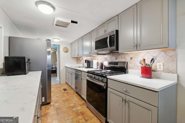 kitchen featuring appliances with stainless steel finishes, gray cabinets, sink, and backsplash