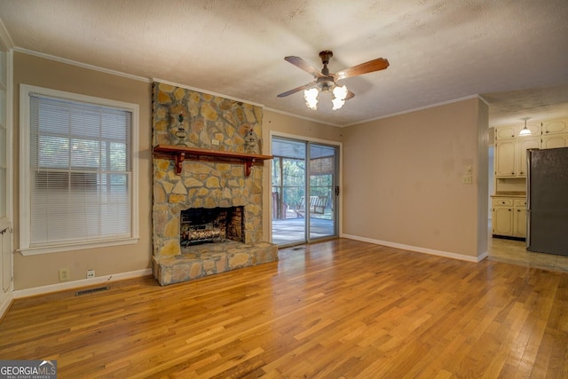 unfurnished living room with a stone fireplace, ceiling fan, crown molding, a textured ceiling, and light hardwood / wood-style flooring