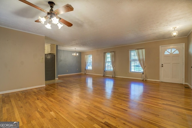 unfurnished living room with ceiling fan with notable chandelier, ornamental molding, a textured ceiling, and light wood-type flooring