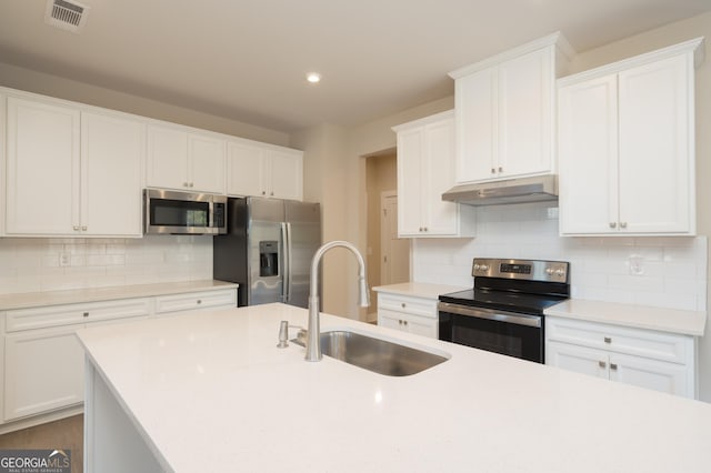 kitchen featuring sink, white cabinetry, stainless steel appliances, tasteful backsplash, and a center island with sink