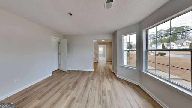 unfurnished room featuring a wealth of natural light, a textured ceiling, and light wood-type flooring