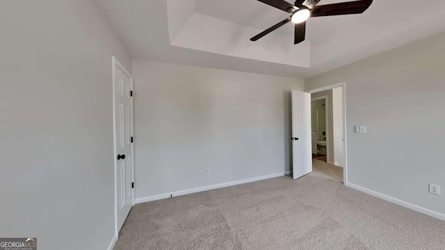 unfurnished room featuring a raised ceiling, light carpet, and ceiling fan