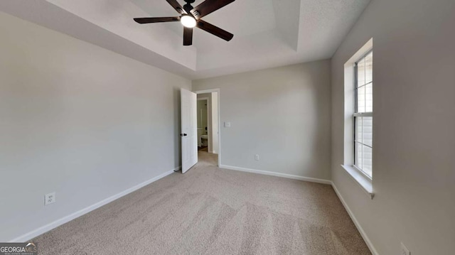 unfurnished room with light carpet, ceiling fan, and a tray ceiling