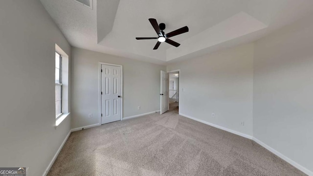 unfurnished bedroom featuring light carpet, ceiling fan, and a tray ceiling