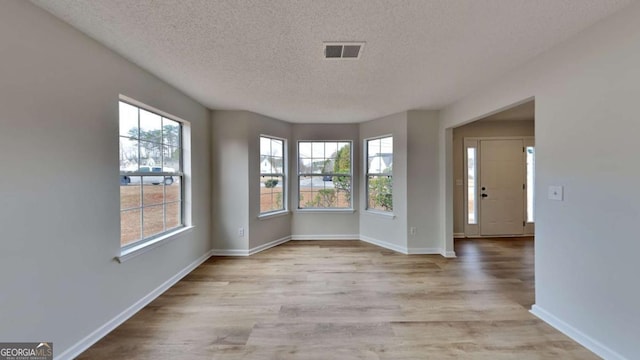 unfurnished room with plenty of natural light, light hardwood / wood-style floors, and a textured ceiling