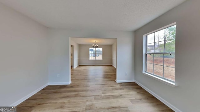 unfurnished room featuring an inviting chandelier, a textured ceiling, and light wood-type flooring