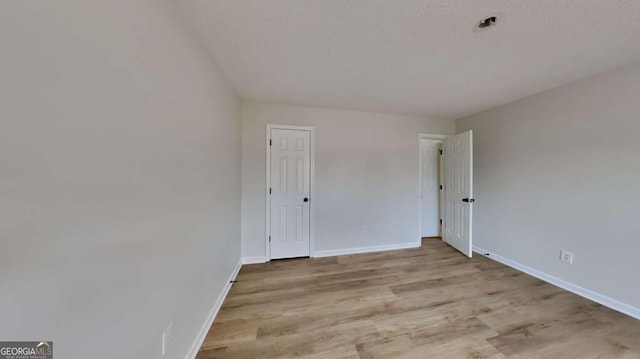 unfurnished room with a textured ceiling and light wood-type flooring