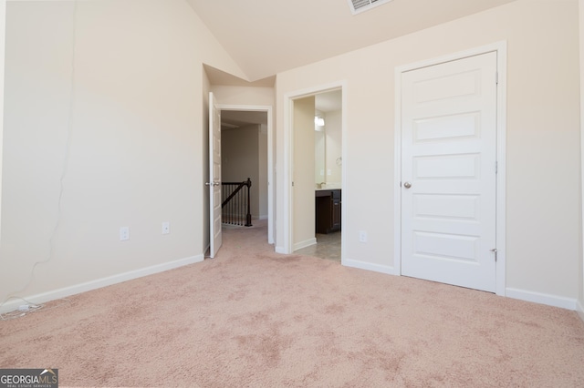 unfurnished bedroom featuring vaulted ceiling, light colored carpet, and ensuite bathroom