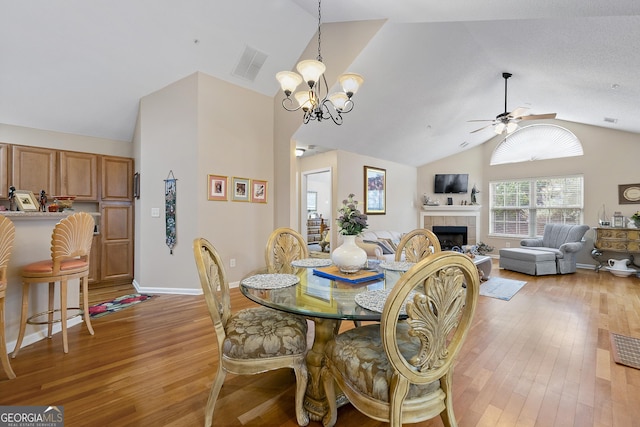 dining room with a tiled fireplace, ceiling fan with notable chandelier, light hardwood / wood-style flooring, and lofted ceiling