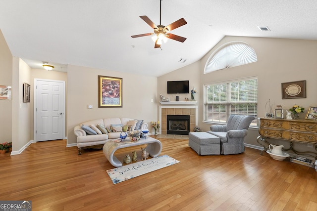 living room featuring a tile fireplace, wood-type flooring, lofted ceiling, and ceiling fan