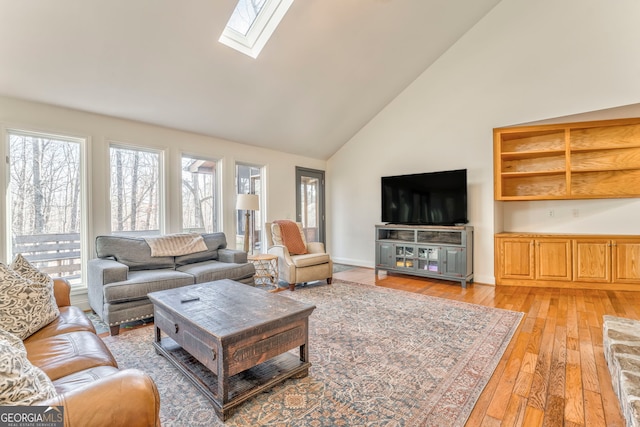 living room featuring light hardwood / wood-style flooring, a skylight, and high vaulted ceiling