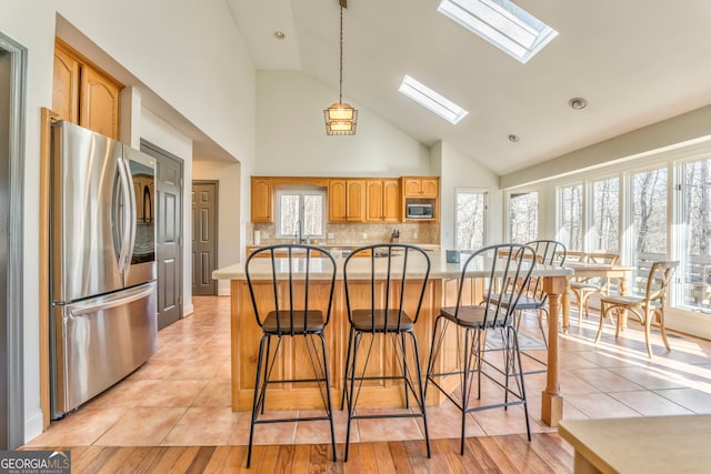 kitchen featuring a skylight, light tile patterned floors, a kitchen island, stainless steel appliances, and backsplash