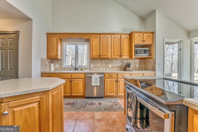 kitchen with appliances with stainless steel finishes, high vaulted ceiling, sink, decorative backsplash, and light tile patterned floors